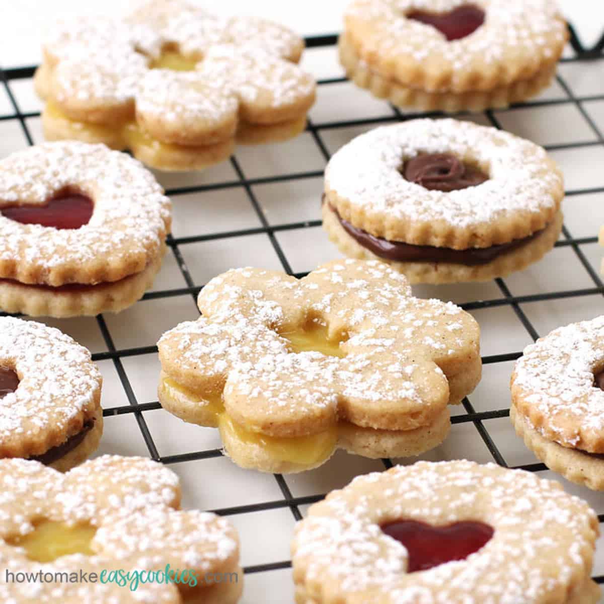 Heart-shaped, daisy-shaped, and round Linzer Cookies filled with raspberry jam, lemon curd, and chocolate hazelnut spread.