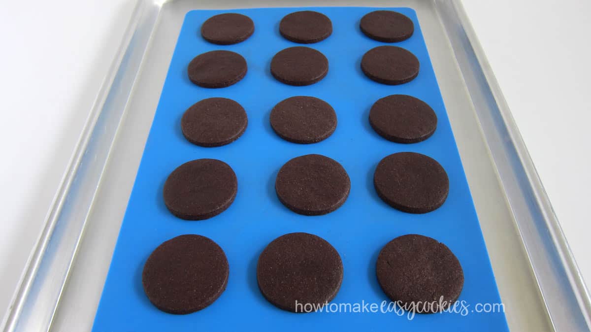 Round chocolate cookies baked on a blue silicone mat on a cookie sheet. 