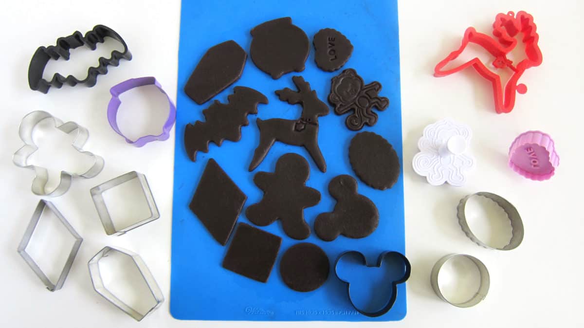 chocolate cut-out cookies on a silicone mat with shaped cookie cutters and plunger cutters