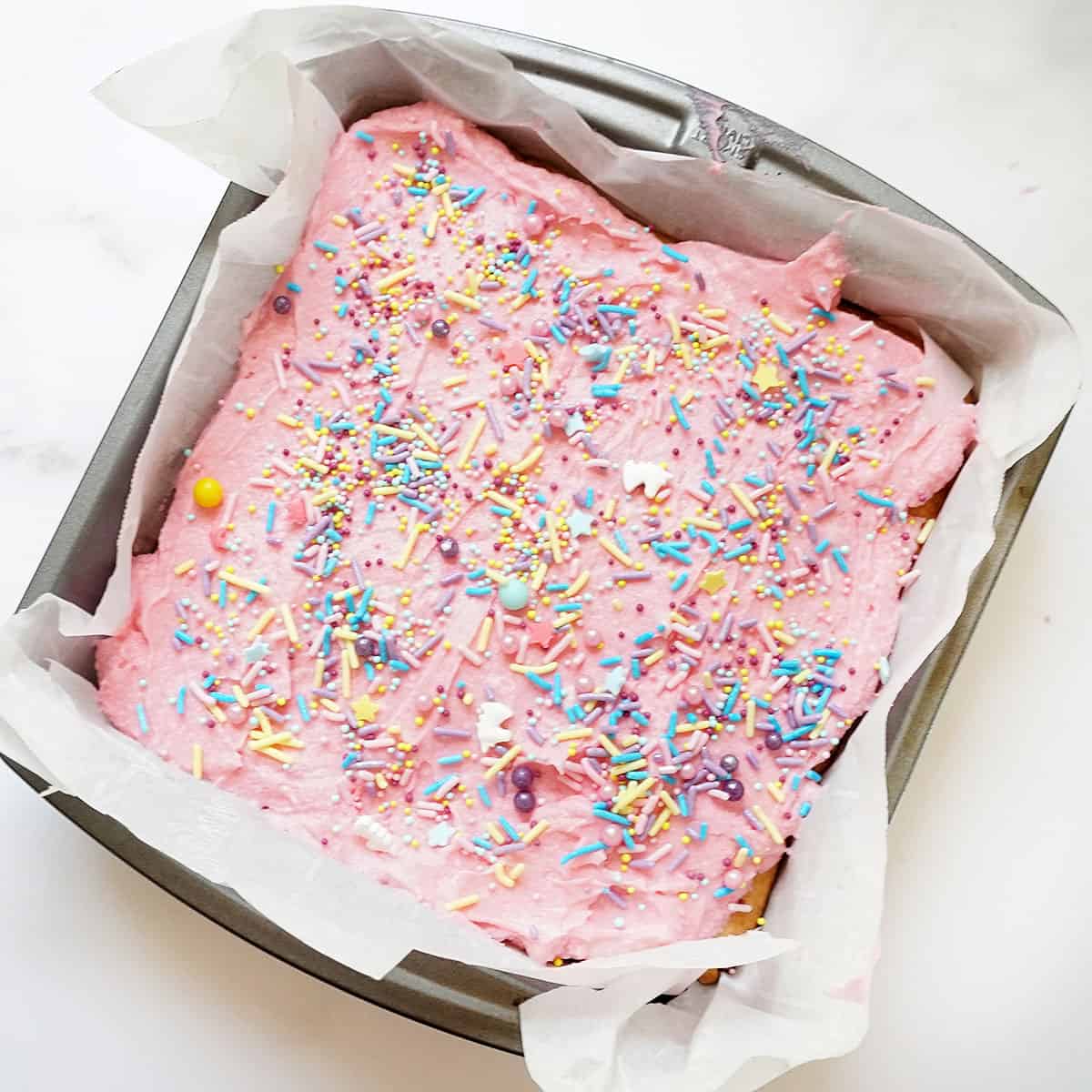 sugar cookie bars with pink frosting and sprinkles in baking pan