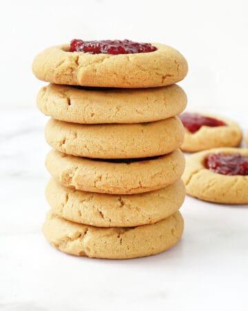 stack of peanut butter thumbprint cookies with raspberry jam