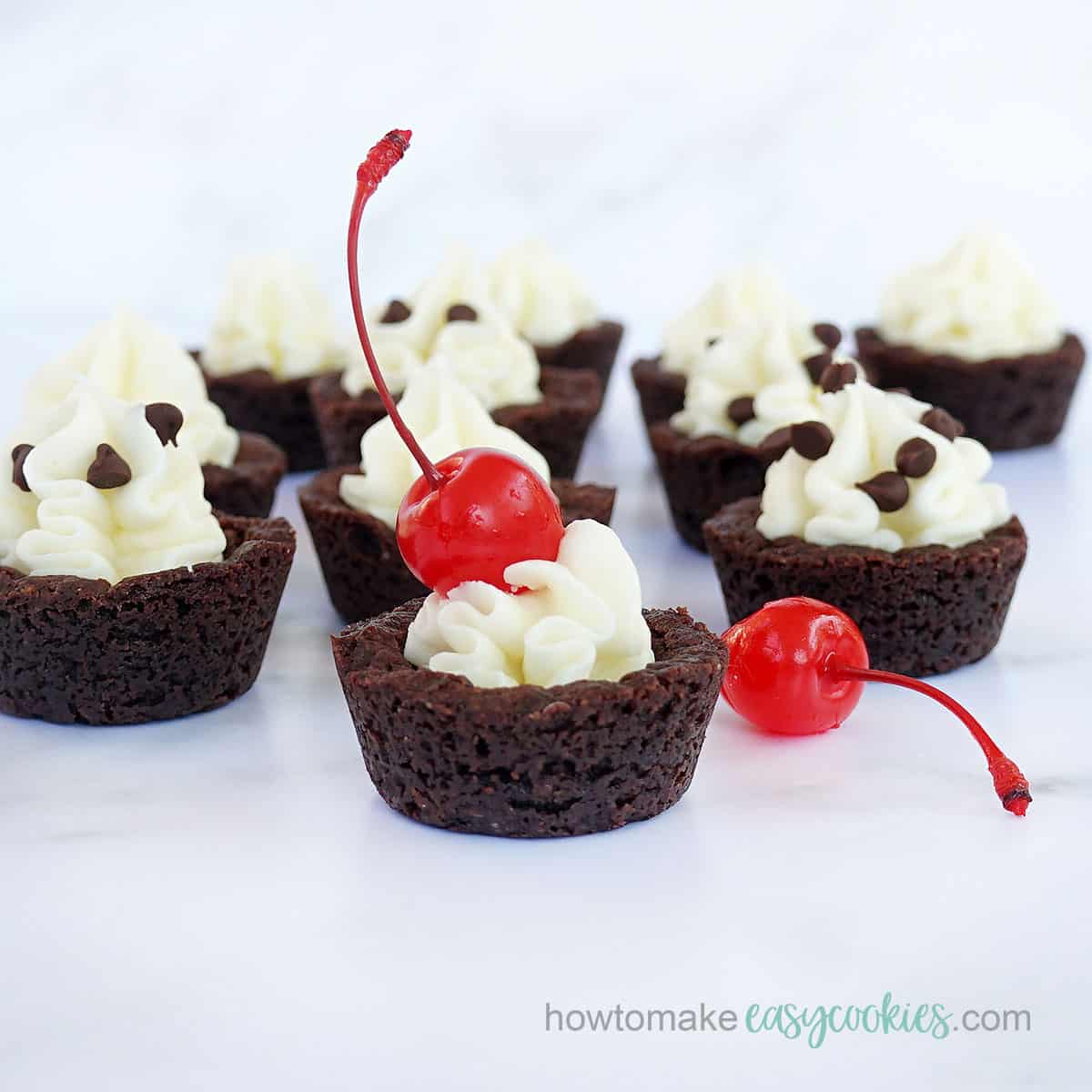 chocolate cookie cups with cream cheese frosting, maraschino cherries and mini chocolate chips