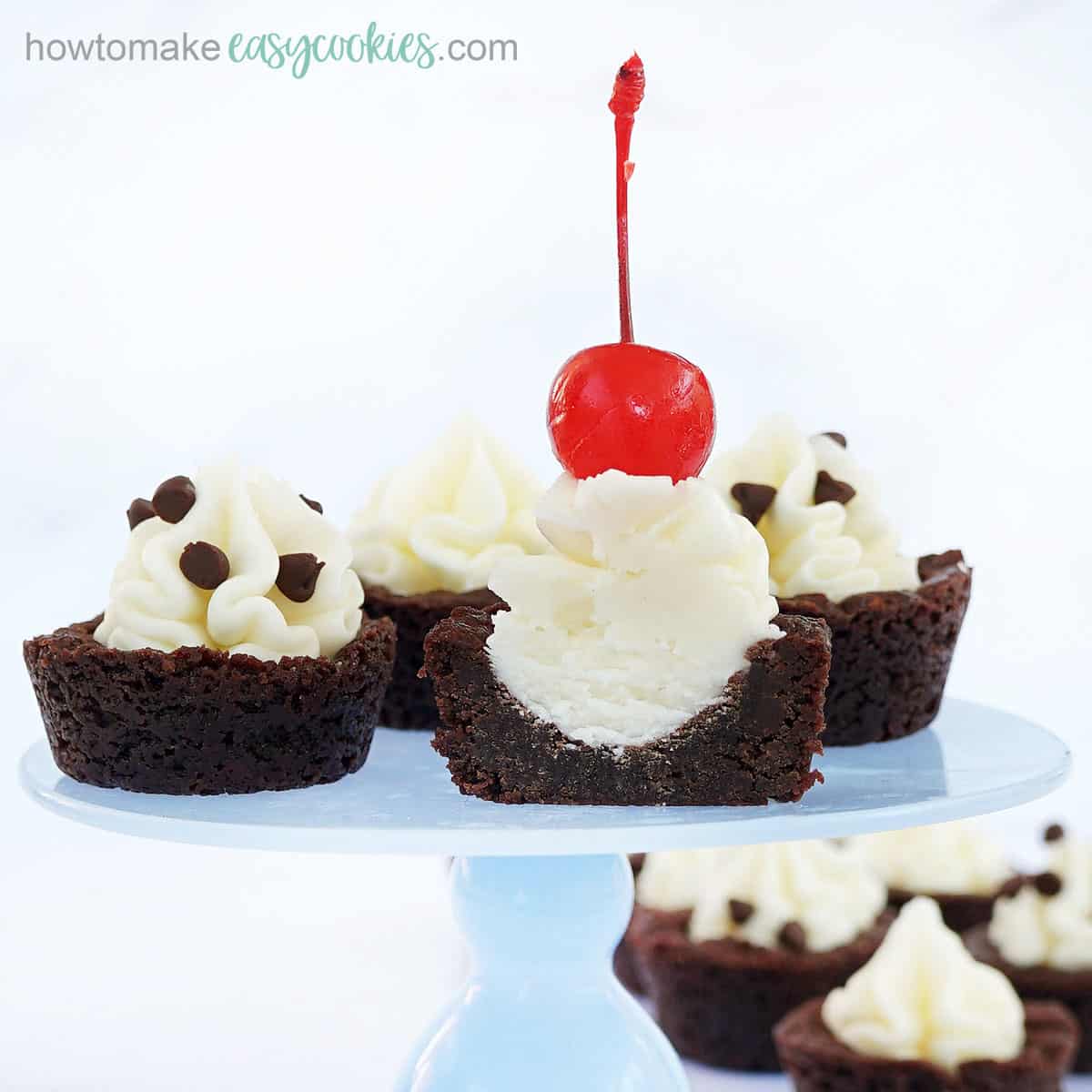 brownie cups filled with cream cheese frosting and topped with chocolate chips and cherries