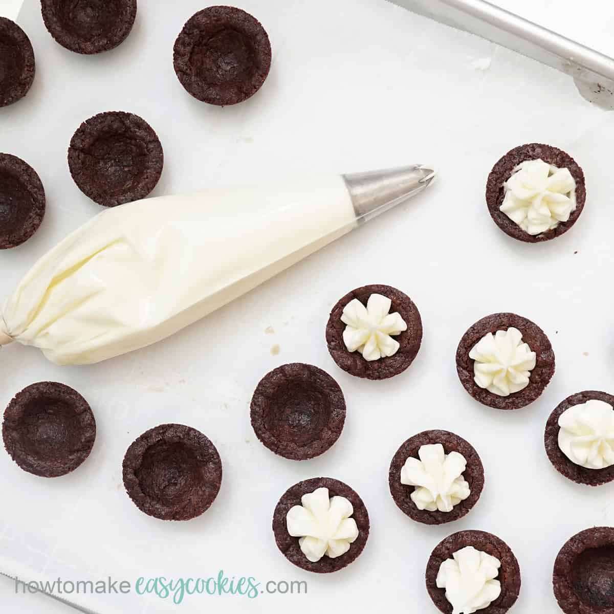 piping cream cheese frosting in chocolate cookie cups