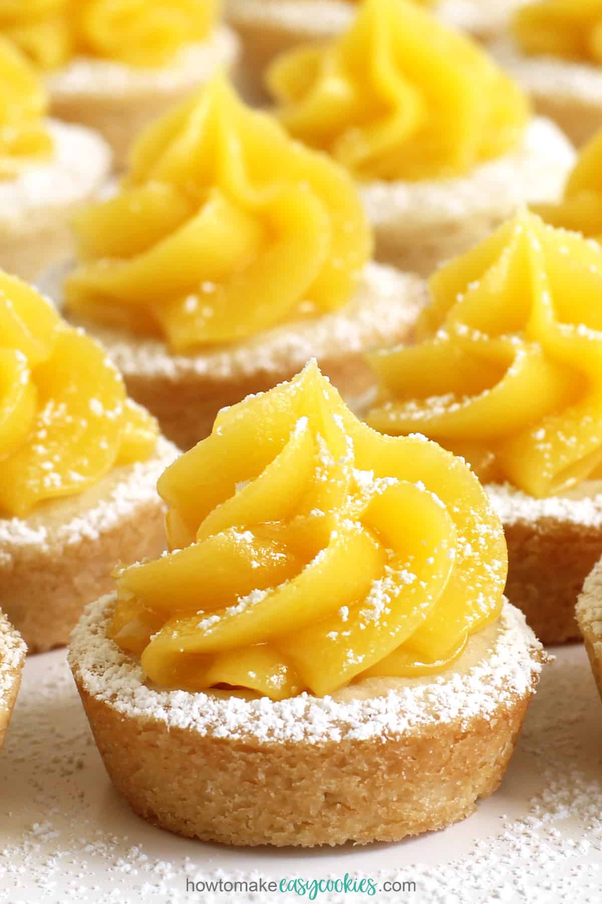 lemon bar cookie cups with a shortbread cookie topped with a swirl of lemon curd and a dusting of powdered sugar