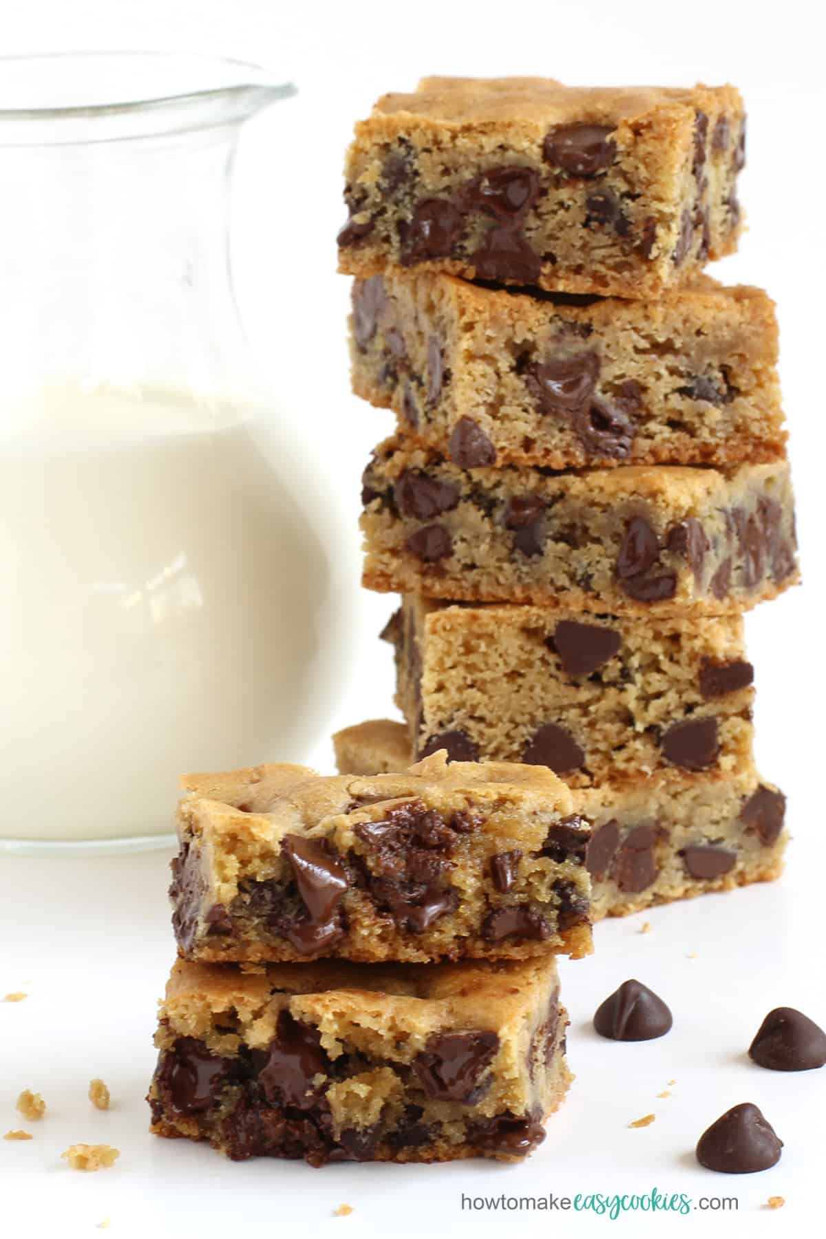 chocolate chip cookie bars stacked next to a pitcher of milk