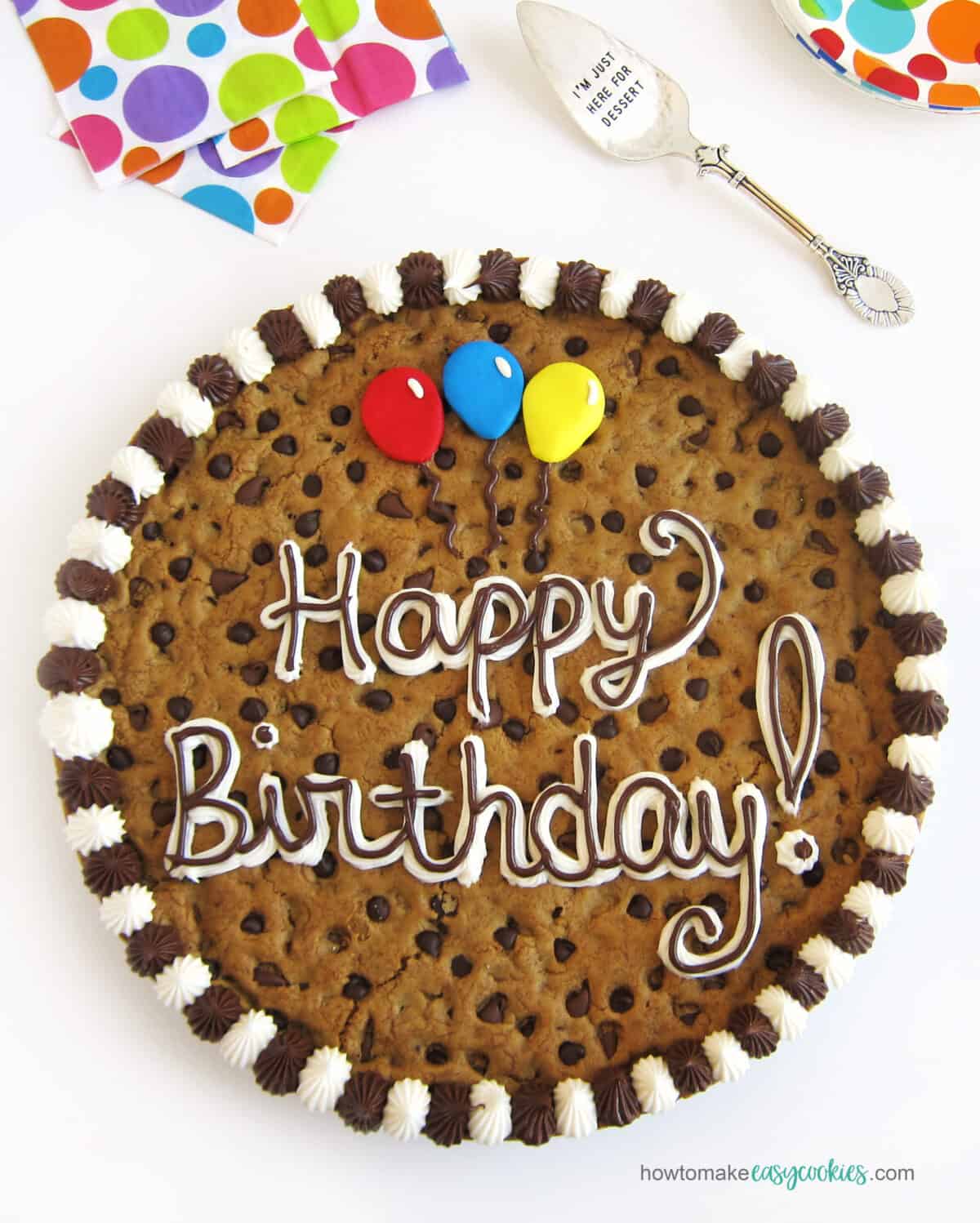 Chocolate chip birthday cookie cake decorated with "Happy birthday" and balloons in frosting.