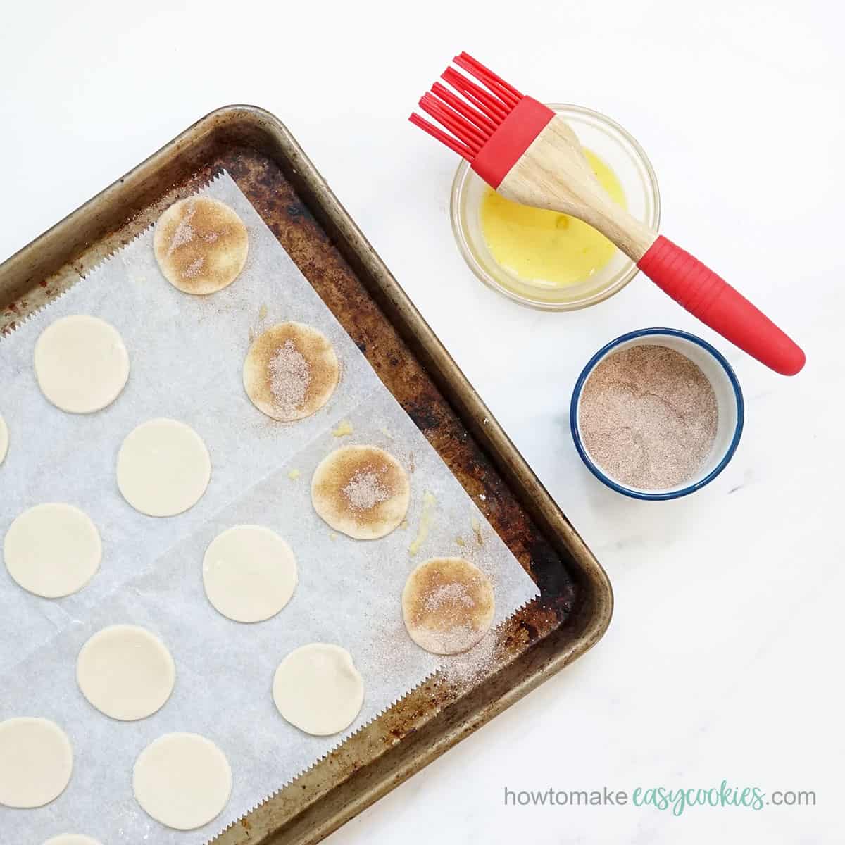 brushing egg wash on pie crust cookies and topping with cinnamon sugar