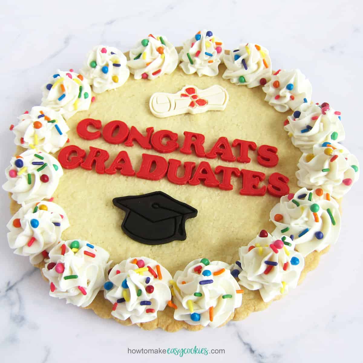 graduation cookie cake topped with cut-out letters spelling "congrats graduates" and a grad cap and diploma