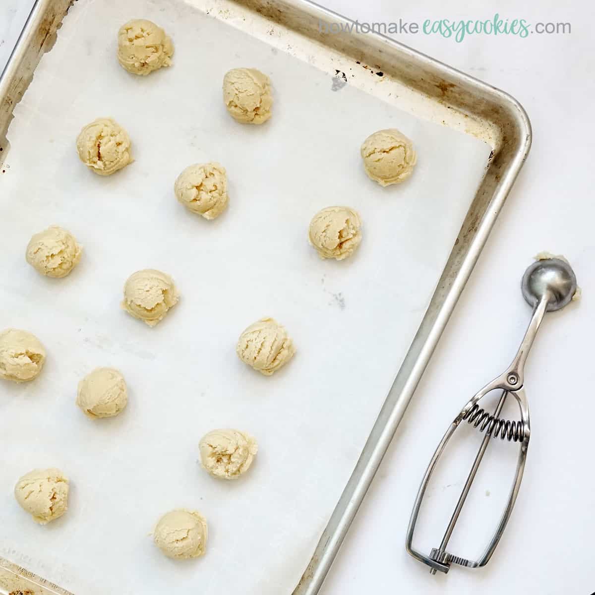 balls of cookie dough on baking tray and cookie scoop