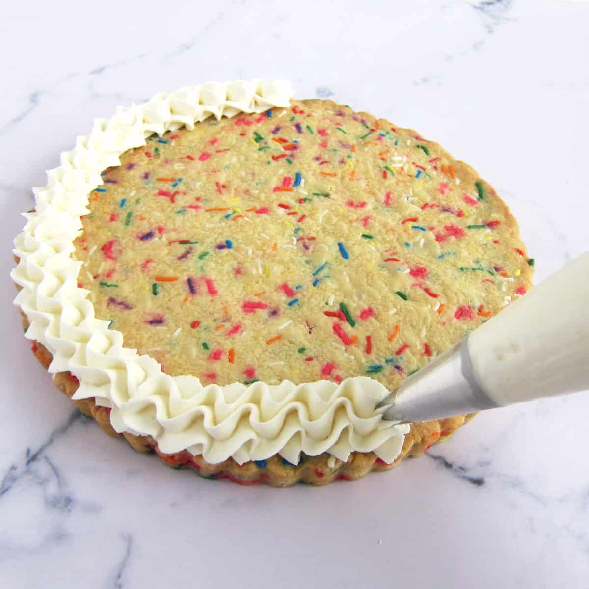 piping frosting on a sugar cookie cake filled with sprinkles