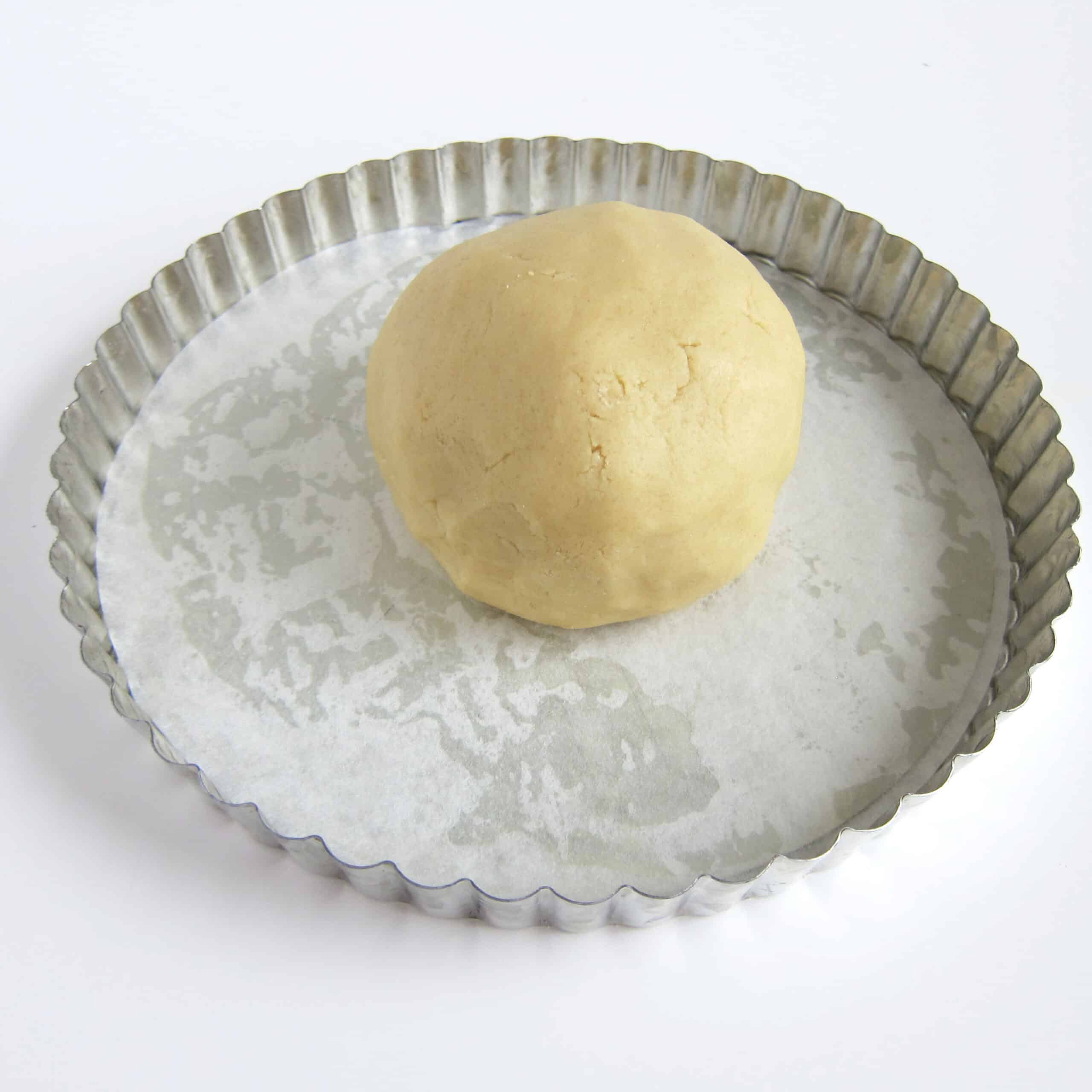 ball of sugar cookie dough in a tart pan lined with parchment paper