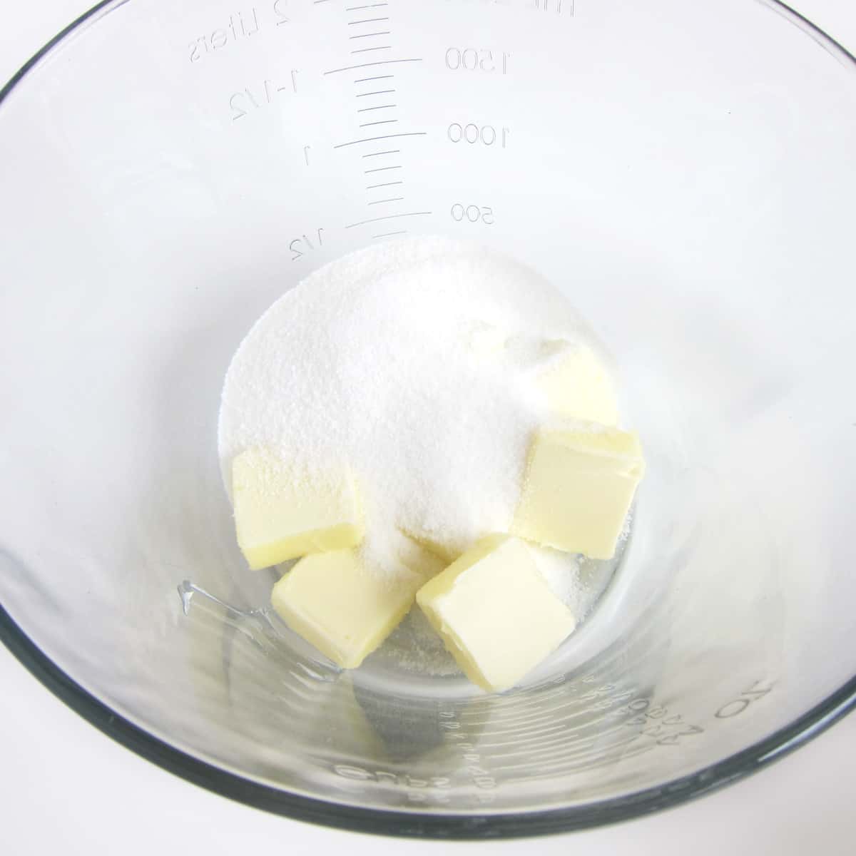 Slices of butter and granulated sugar in a mixing bowl.