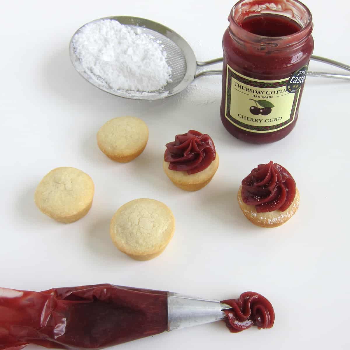 Pipe cherry curd on top of sugar cookie cups then dust with powdered sugar.