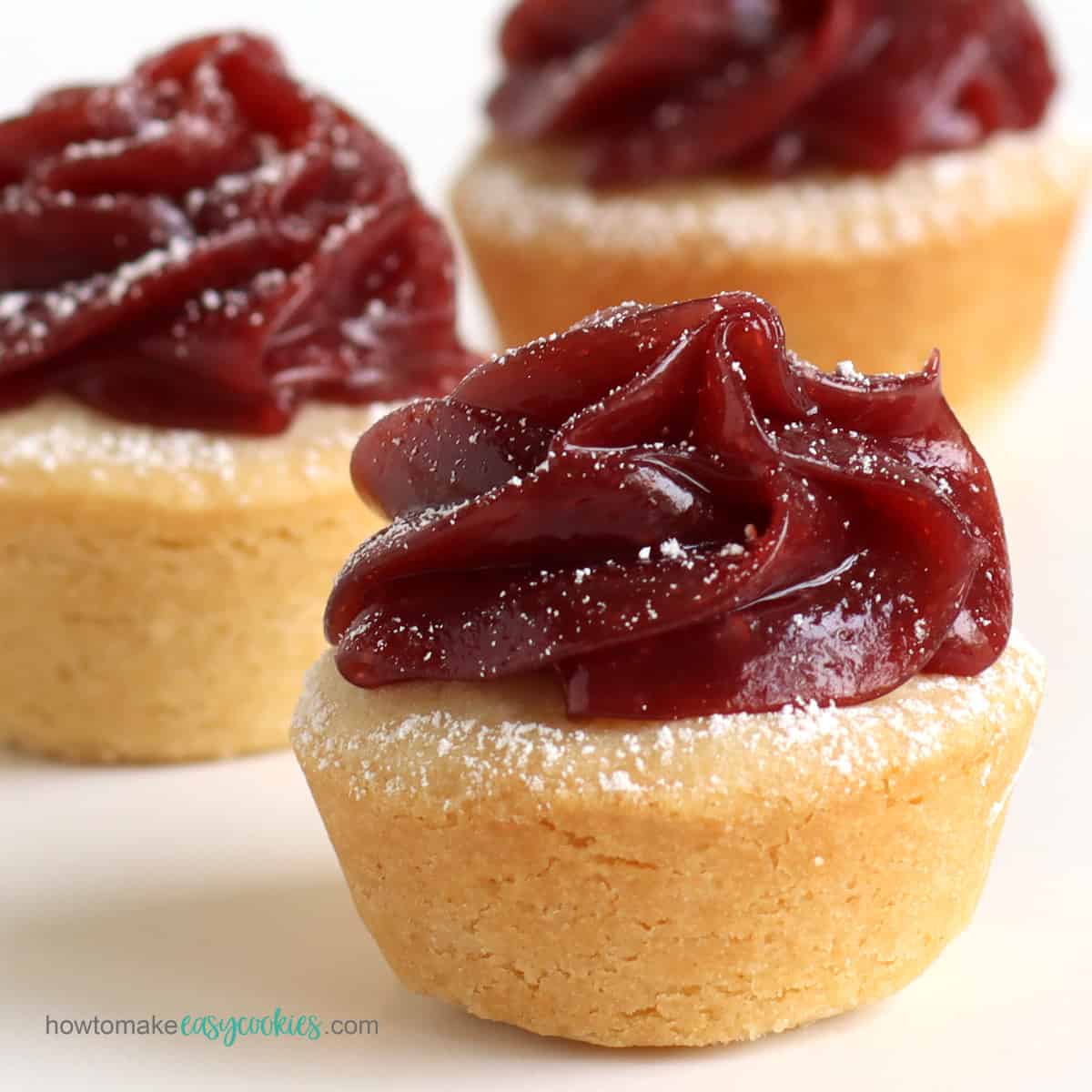 Swirls of cherry curd on top of sugar cookie cups dusted with powdered sugar.