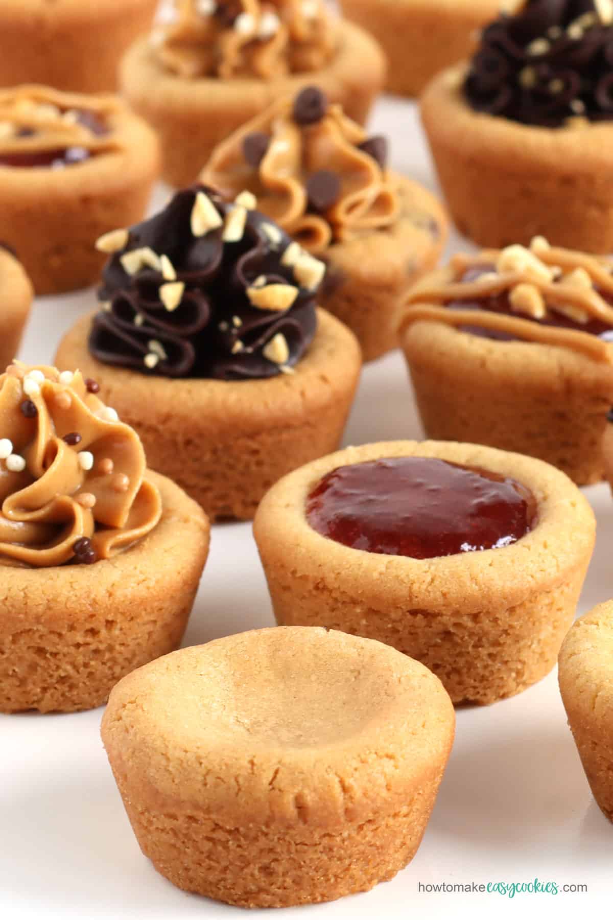 peanut butter cookie cups topped with strawberry jam, peanut butter, and chocolate frosting