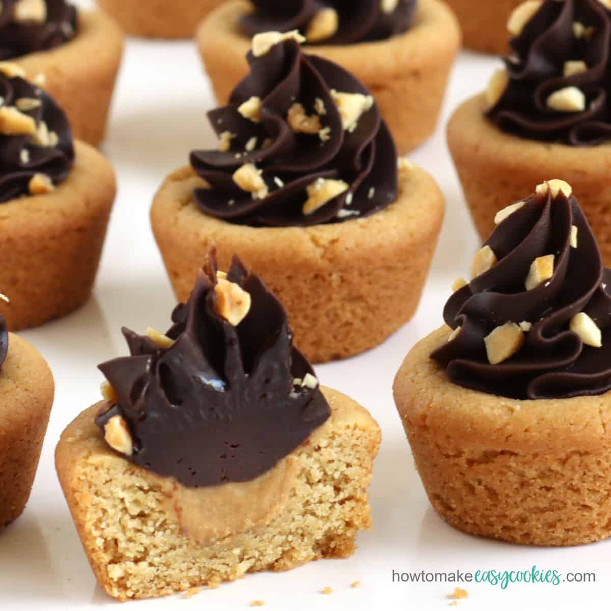 peanut butter cookie cups filled with peanut butter and topped with chocolate ganache frosting and chopped peanuts