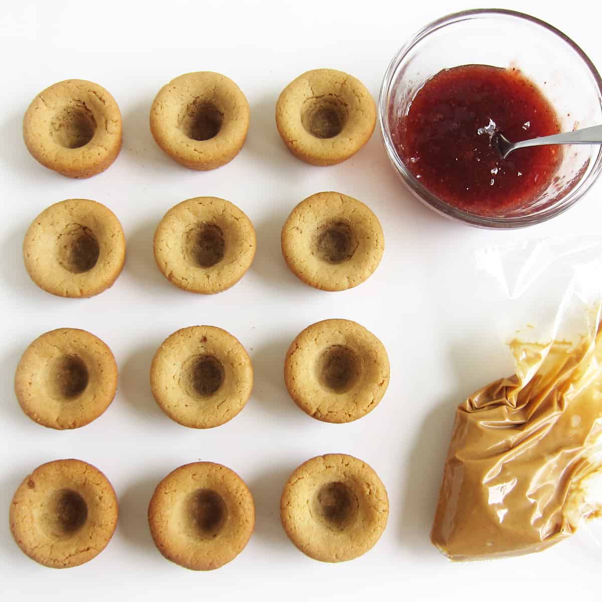 peanut butter cookie cups with indentations, with strawberry jam and a bag of peanut butter