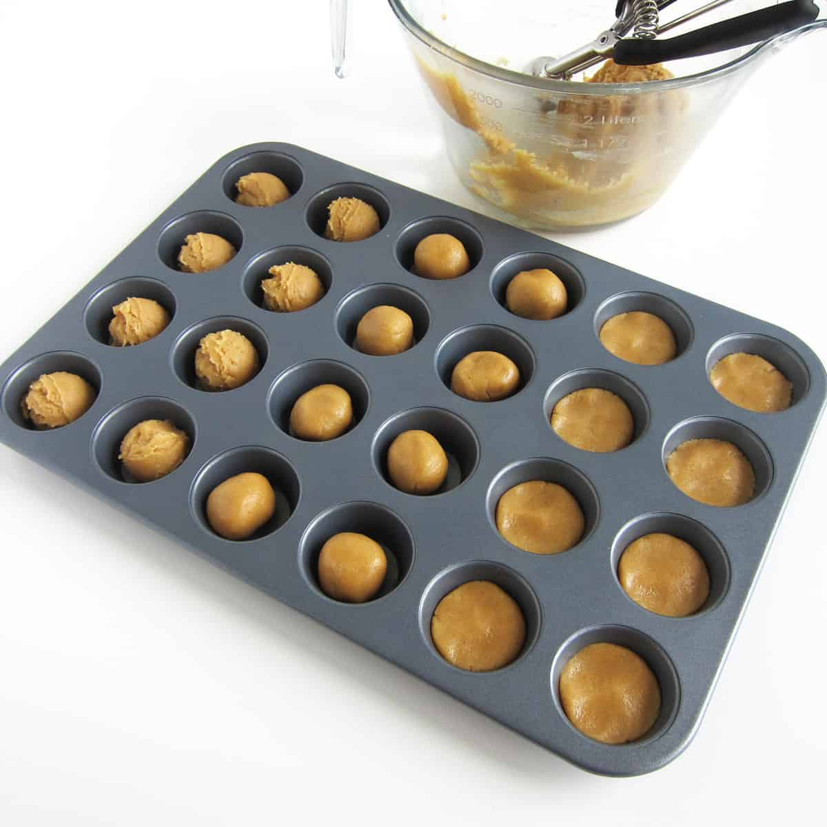 Mini muffin cup filled with peanut butter fudge scoops, balls, and flattened balls.