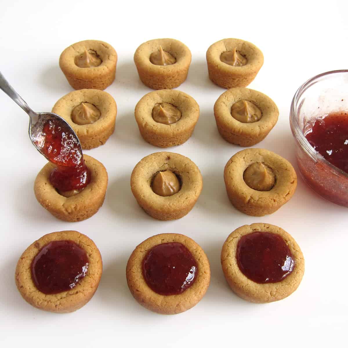 spooning strawberry jam over the peanut butter cookie cups filled with peanut butter