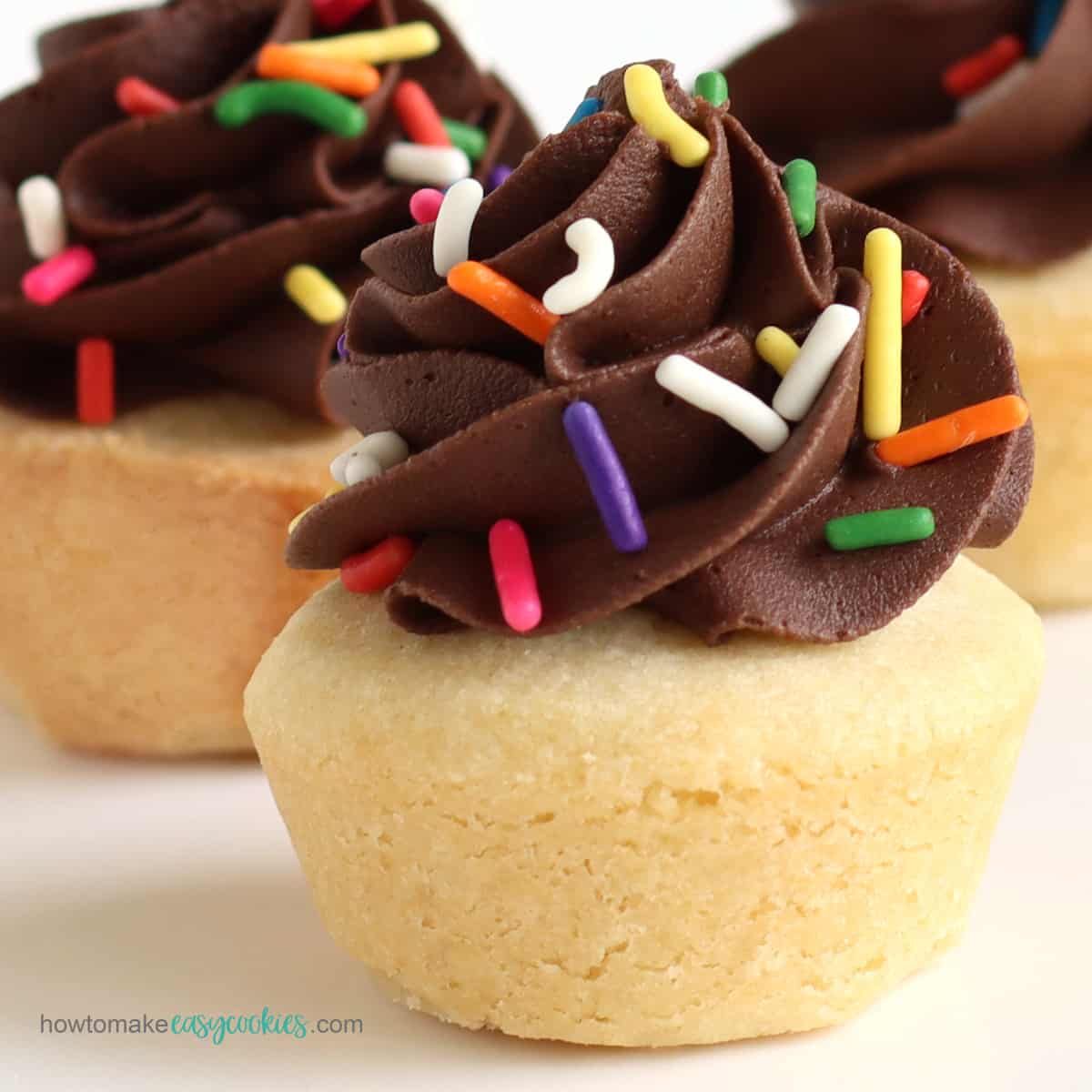 Sugar cookie cups topped with a big swirl of chocolate frosting and rainbow sprinkles.