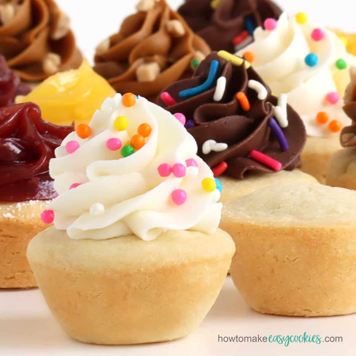 Sugar cookie cups topped with swirls of vanilla frosting with colorful Crispearls, chocolate frosting with rainbow sprinkles, lemon curd, cherry curd, and Biscoff spread.