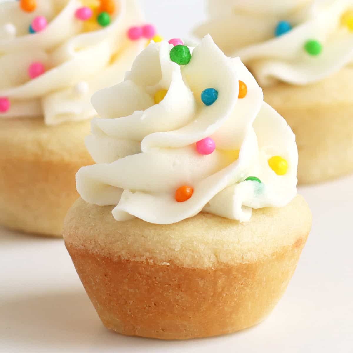A big swirl of vanilla frosting and rainbow Crispearls on top of bite-sized sugar cookie cups.