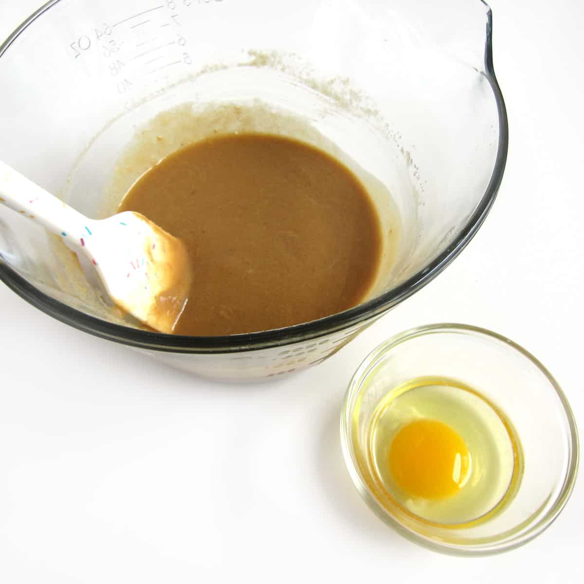 butter, brown sugar, granulated sugar, and peanut butter mixed together in a mixing bowl next to a cracked egg in a bowl.